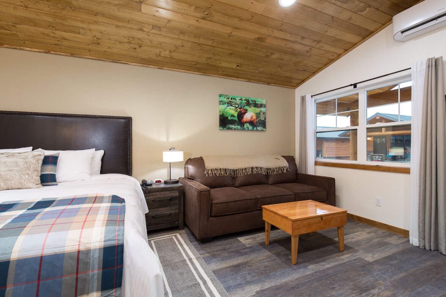 Une chambre à coucher avec un lit, une table de chevet, un canapé marron, une table basse en bois et une fenêtre avec des rideaux.