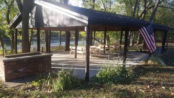 Un espace pique-nique abrité, équipé de bancs et de tables, avec un drapeau américain et une vue sur un lac.