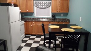 Una cocina compacta con armarios de madera, piso a cuadros, un refrigerador, una cafetera y una mesa de comedor con sillas.