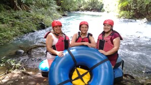 Three people in red helmets and life vests standing by a river with a blue inflatable raft. - Wonderful View Cabins (Bijagua)