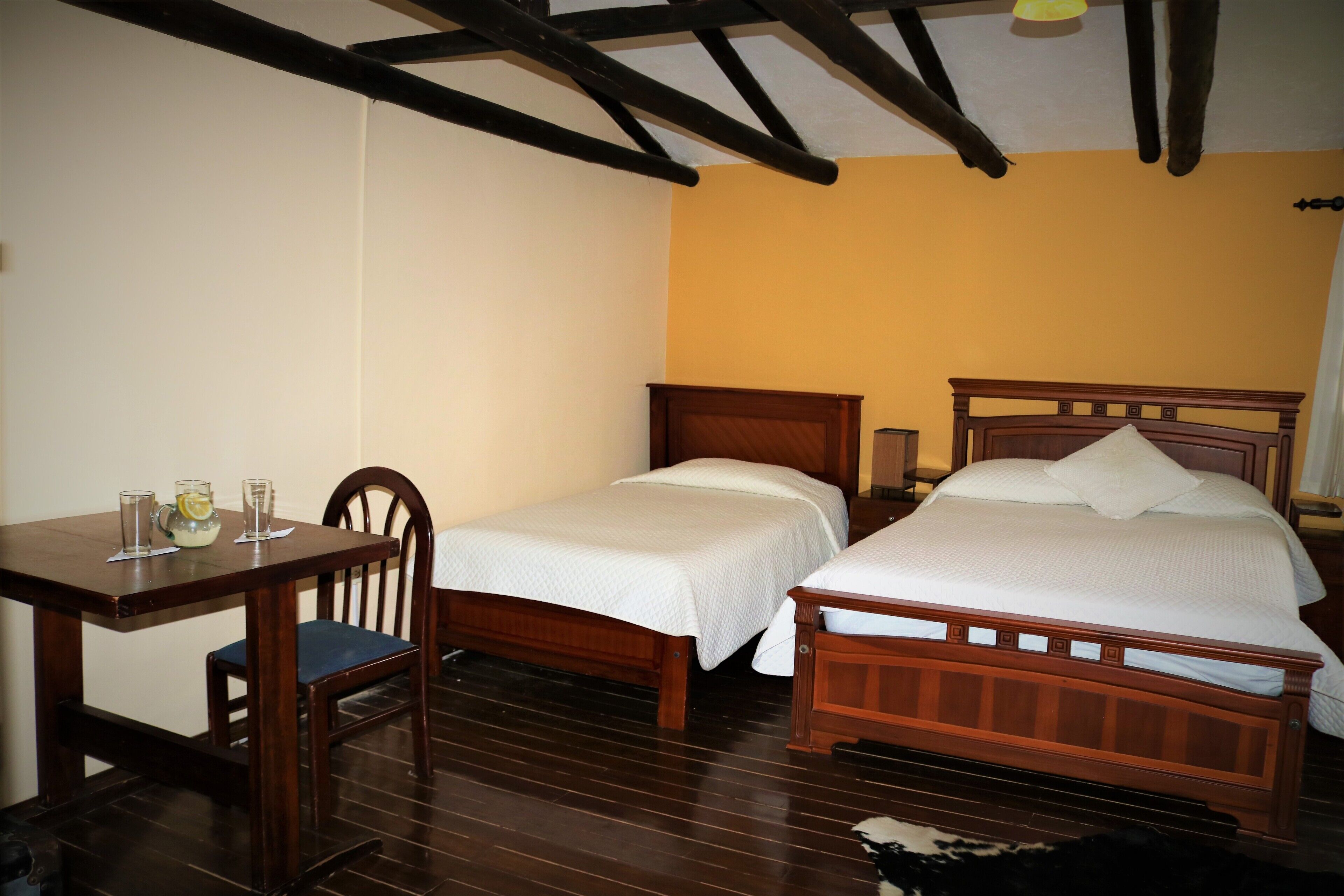 A room with two single beds, a wooden table with chairs, and a small table with glasses and a jug.