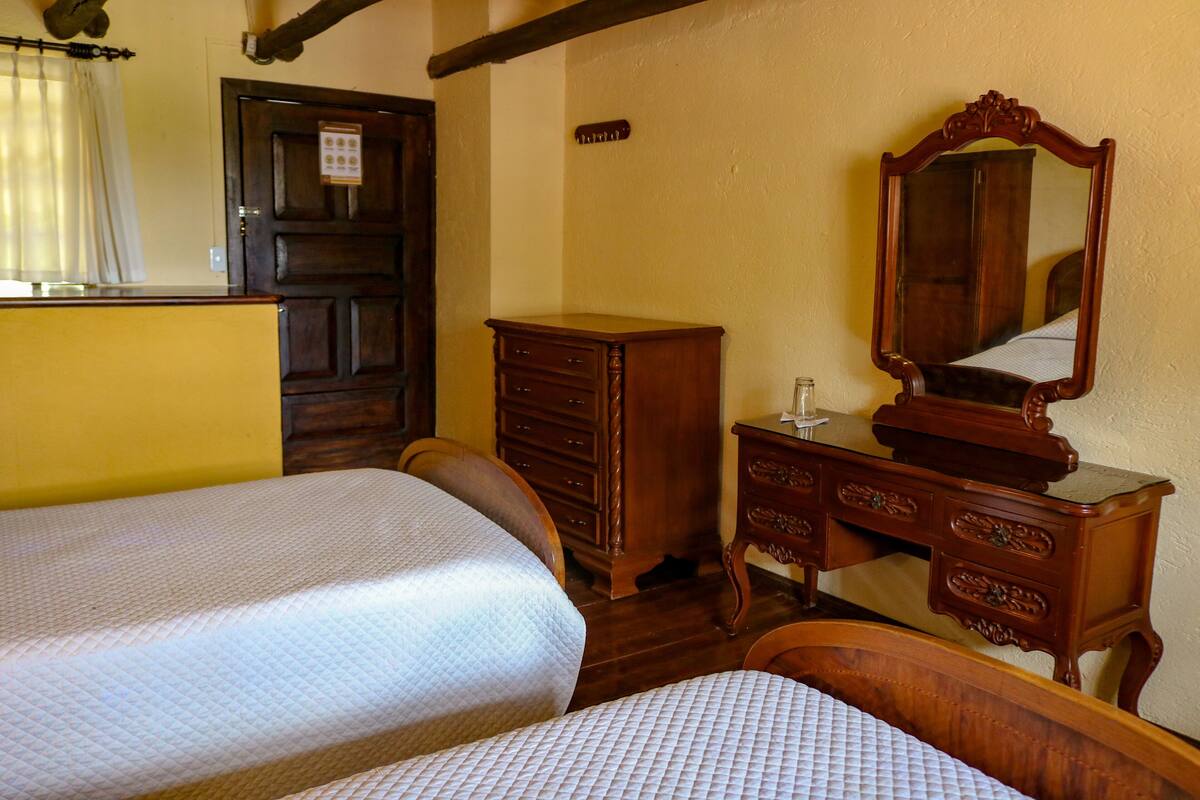 A bedroom with two beds, a wooden dresser, a mirror, and a door with a sign.