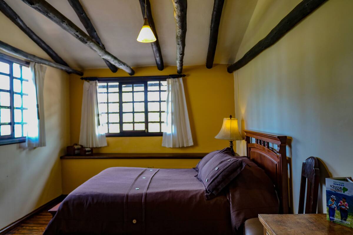 A room with a bed, a window with curtains, a lamp, and a magazine on a table.