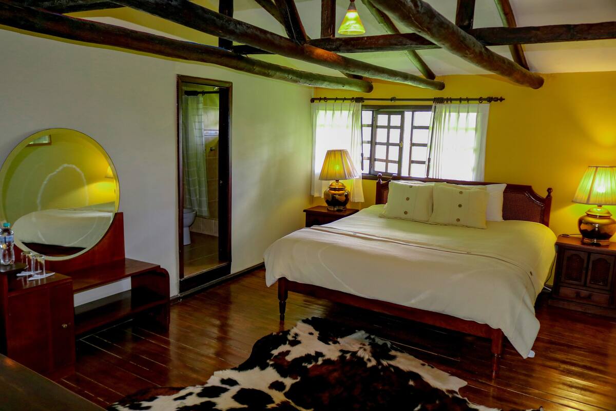 A bedroom with a wooden bed, a round mirror, a wooden nightstand with lamps, and a cowhide rug.