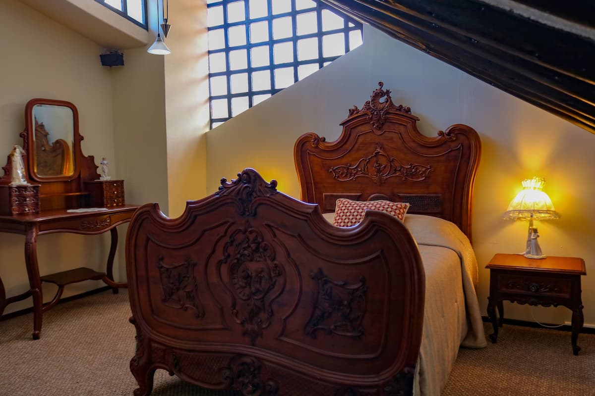 A bedroom with a large bed, a dresser, a mirror, and a nightstand with a lamp.