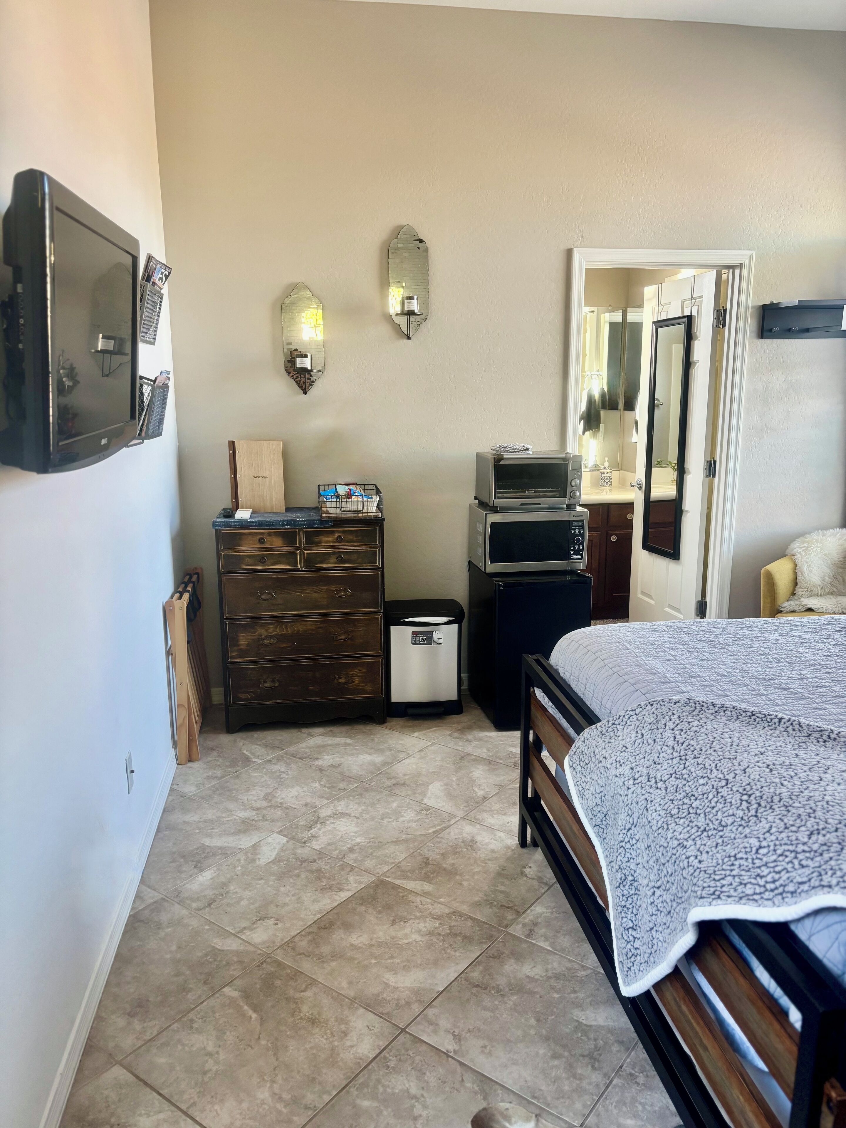 A bedroom with a bed, dresser, microwave, and a door leading to another room.