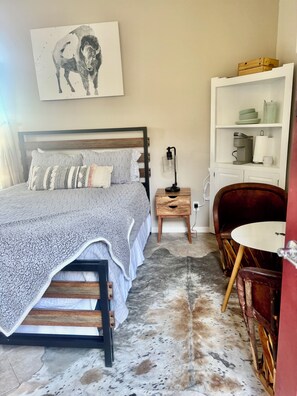 Un dormitorio con cama, mesita de noche, lámpara y una silla roja.
