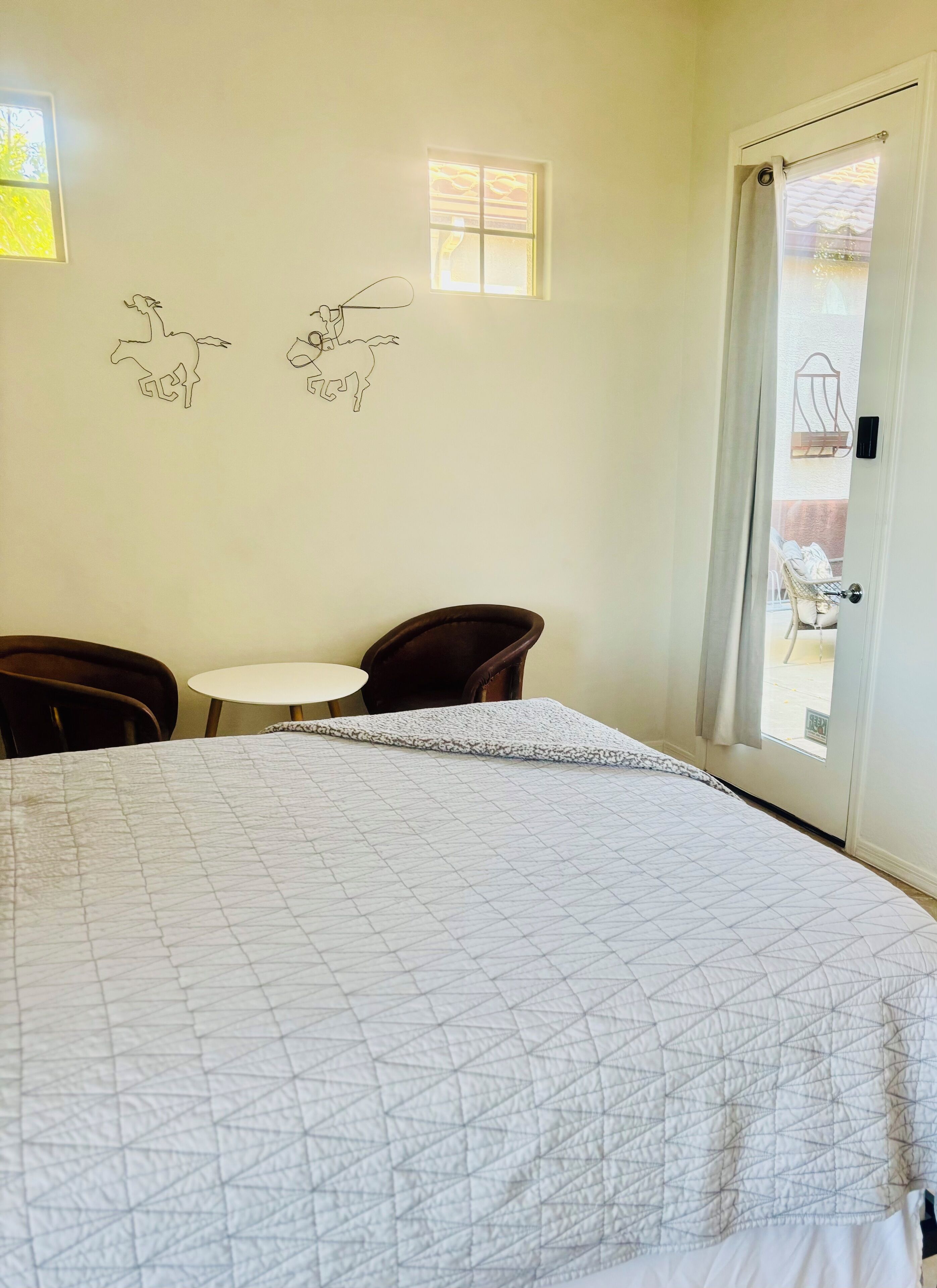 A bedroom with a bed, a small round table, two chairs, and a door leading to a balcony.