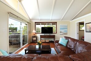 A living room with a brown leather sofa, a flat-screen TV, and a glass door leading to an outdoor area.