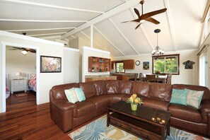 A spacious living room with a brown leather sectional sofa, a coffee table with a vase of flowers, and a ceiling fan. - Spacious Maui Beach House, Private Pool, AC, Sleeps 6 (Kihei)