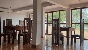 Une salle à manger spacieuse, dotée de hauts plafonds et de grandes fenêtres, qui offre une vue sur l’extérieur.