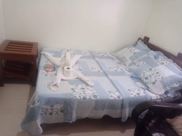 A bed with a floral-patterned bedspread, a wooden nightstand, and a white object on the bed. - Balai Mariacaria Pension House (Guindulman)