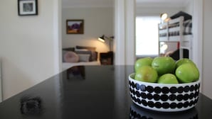 Un bol de pommes vertes sur une table noire, dans une pièce aux murs blancs et dotée d’une fenêtre.