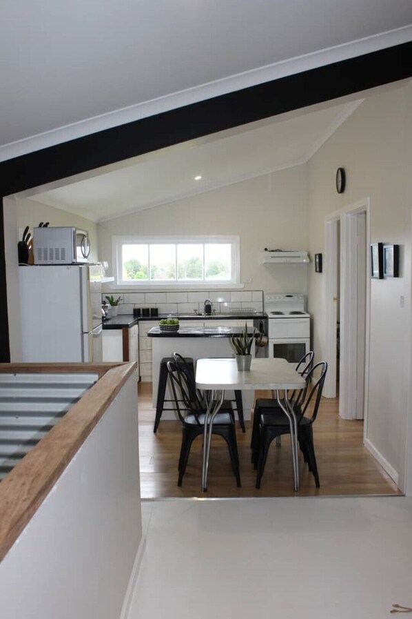 A modern kitchen with white cabinets, a dining area with a table and chairs, and a view of the outdoors through a window.