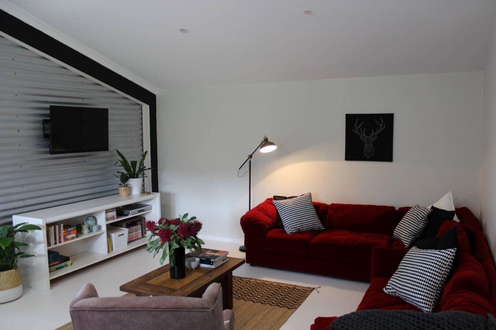 A living room with a red sofa, a coffee table, a bookshelf, and a mounted TV.