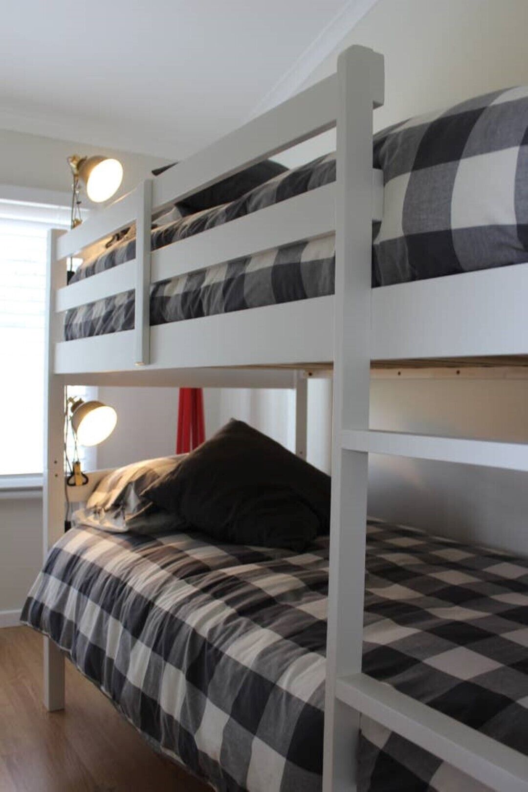 A bunk bed with a checkered bedspread, a red curtain, and a desk lamp.