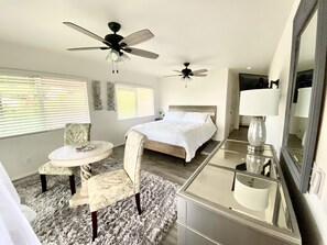 A bedroom with a bed, two ceiling fans, a bedside table with a lamp, a chair, and a large mirror. - Gorgeous Ocean View, Comfortable Cool Elevation, Close to Everything! (Kailua-Kona)