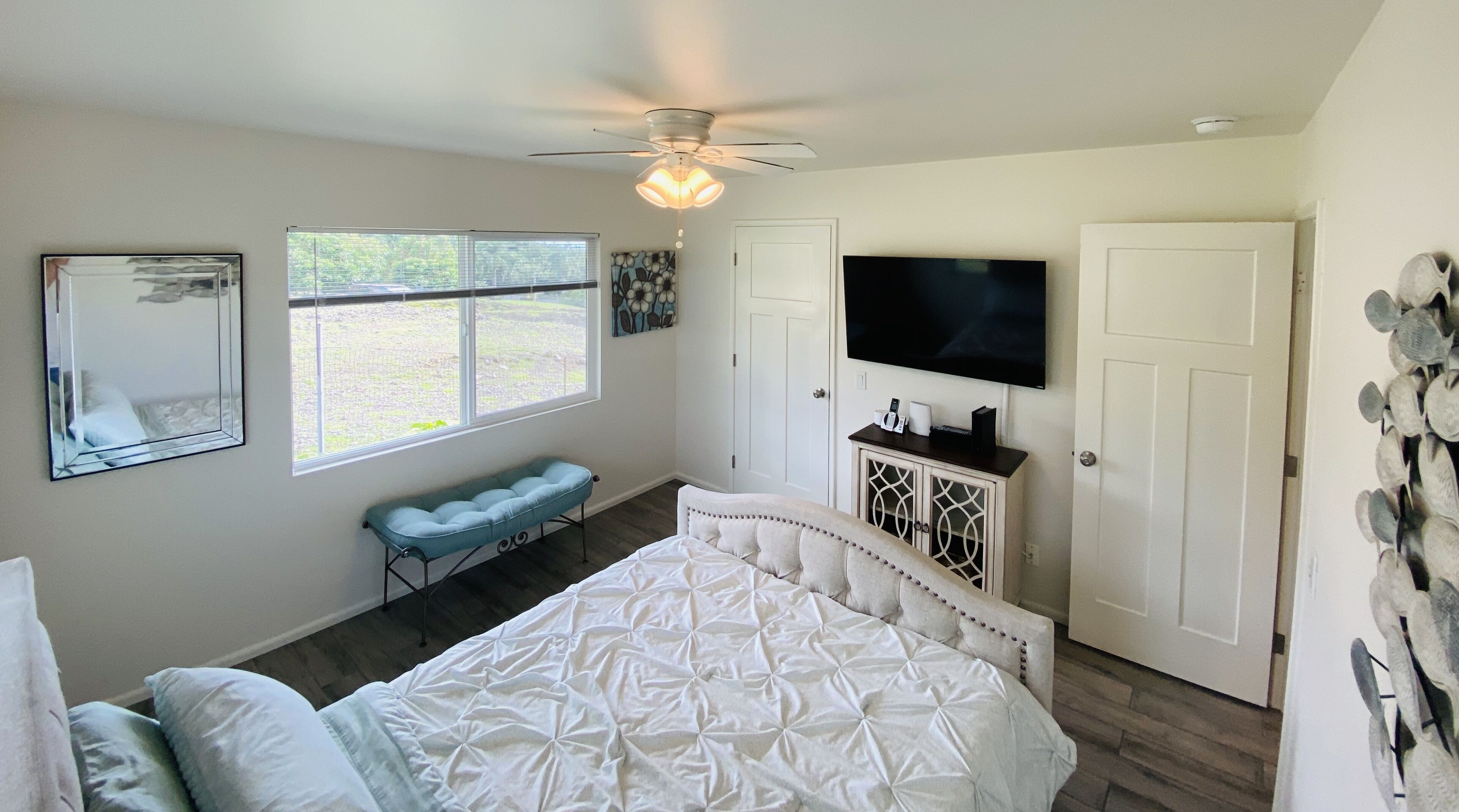 A bedroom with a bed, a bench, a TV, and a ceiling fan.