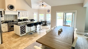A modern kitchen with a central island, a dining area with a large wooden table, and a view of a swimming pool.