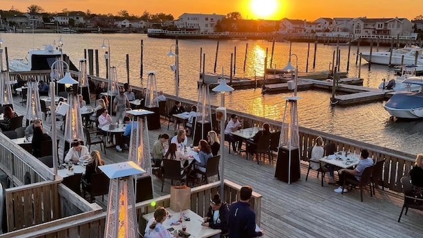 A waterfront restaurant with outdoor seating overlooking the marina and the sunset.