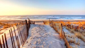 A sandy beach path leading to the ocean with wooden fencing on both sides.