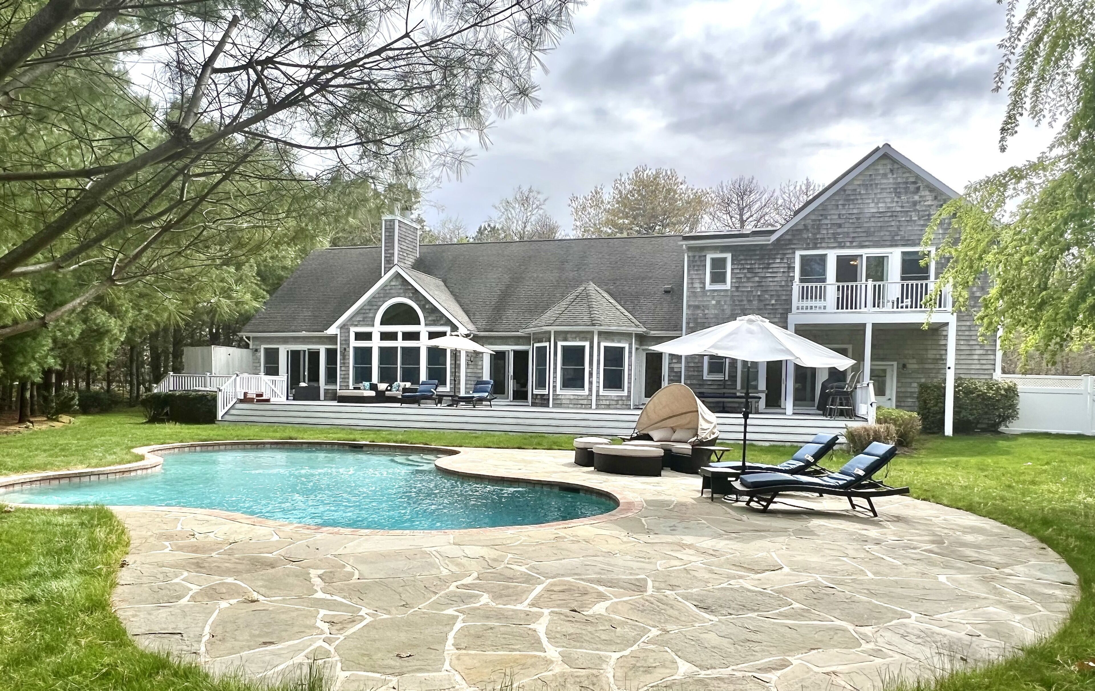 Una casa grande con piscina, patio de piedra y mobiliario exterior.