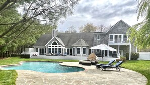 A large house with a swimming pool, stone patio, and outdoor furniture.