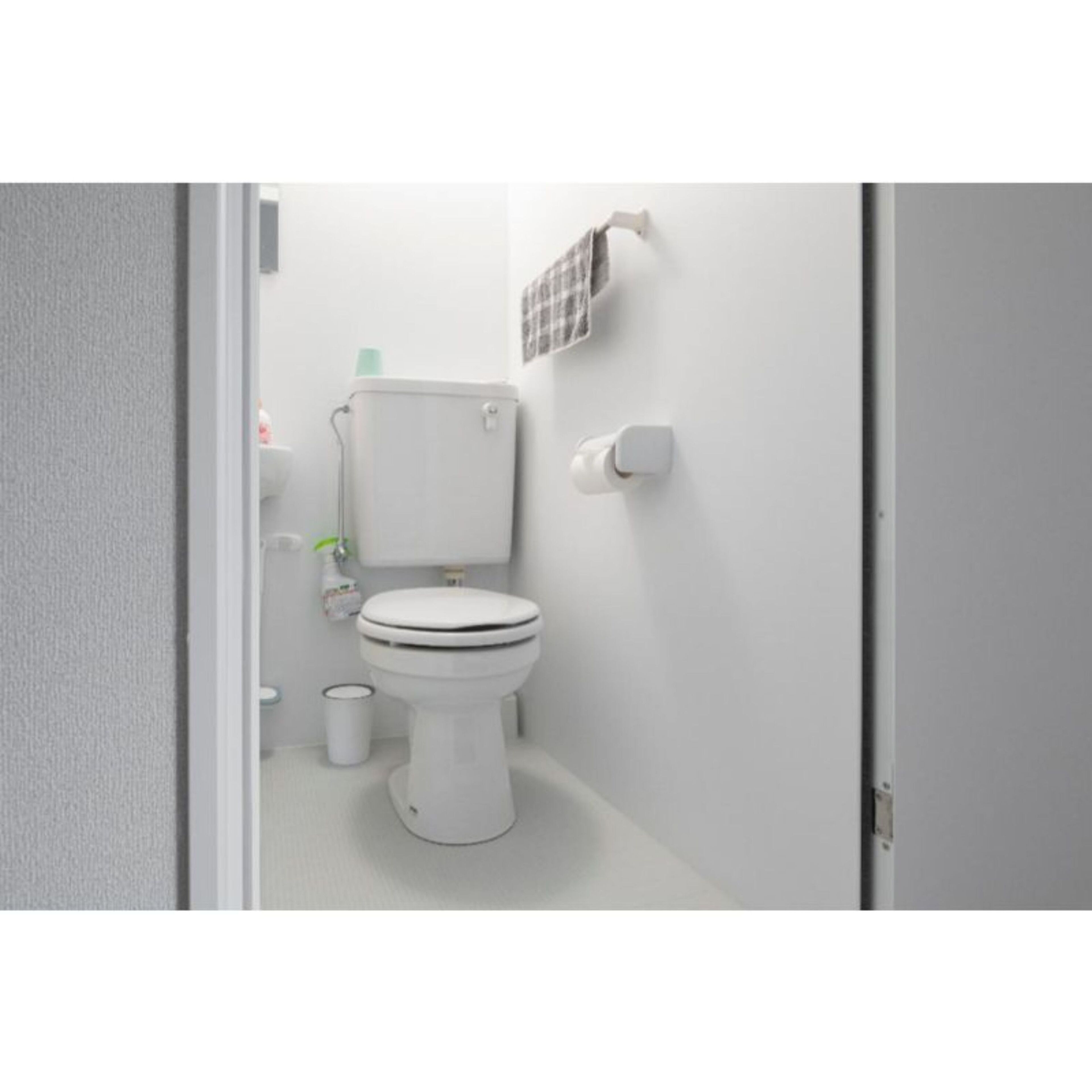 Un baño pequeño y limpio con inodoro, un bote de basura y un portaescobillas en la pared.