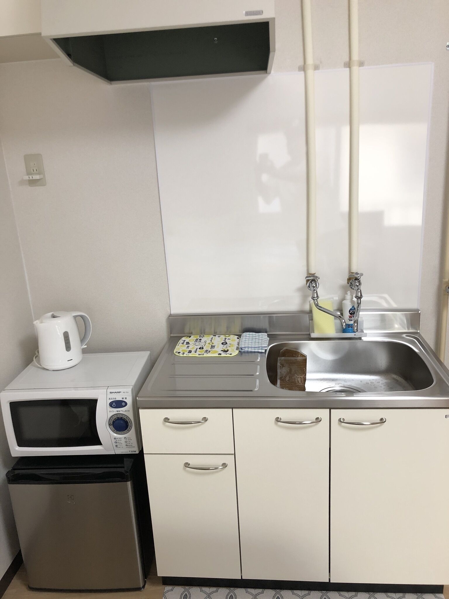 A compact kitchenette with a microwave, a small refrigerator, a sink, and a kettle.