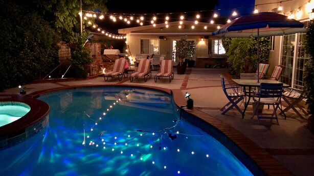 Un espace piscine doté d’un jacuzzi, de chaises longues et de guirlandes lumineuses.