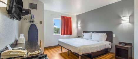 Una habitación de hotel con cama, mesita de noche, escritorio con teléfono y televisión en la pared.