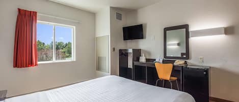 Hotelkamer met een bed, bureau, stoel, televisie en raam met gordijnen.