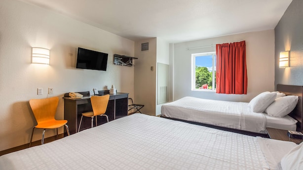 Une chambre d’hôtel avec deux lits, un bureau avec des chaises, un téléviseur fixé au mur et une fenêtre avec des rideaux.
