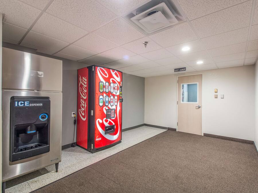 Corredor com dispensador de gelo, máquina de refrigerantes Coca-Cola e área de lavanderia para hóspedes.
