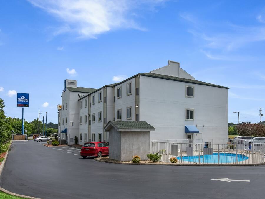Un hotel de varios pisos con piscina, estacionamiento y un letrero que indica un restaurante cercano.