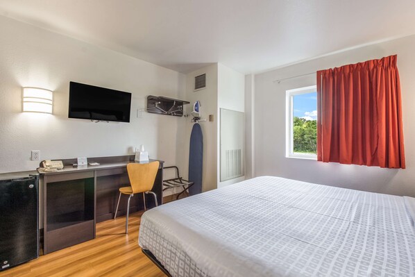 A hotel room with a bed, a desk, a chair, a TV, and a window with curtains.