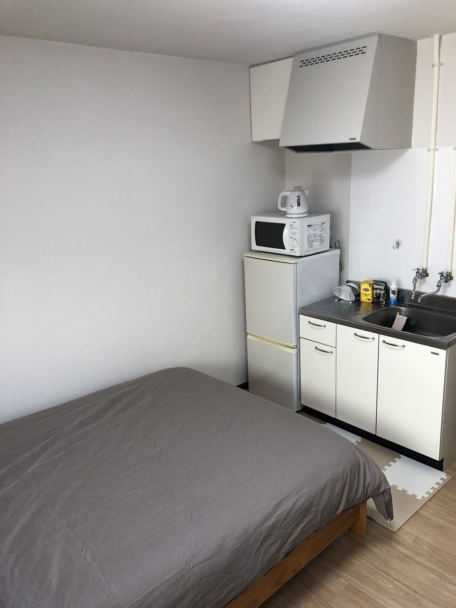 Una camera da letto compatta con un letto, angolo cottura con microonde, piccolo frigorifero e lavello.