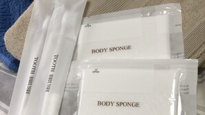 A bed with a striped bedspread, two towels, and two packages labeled "TOOTH BRUSH" and "BODY SPONGE". - Sapporo Apartment 105 (Sapporo)