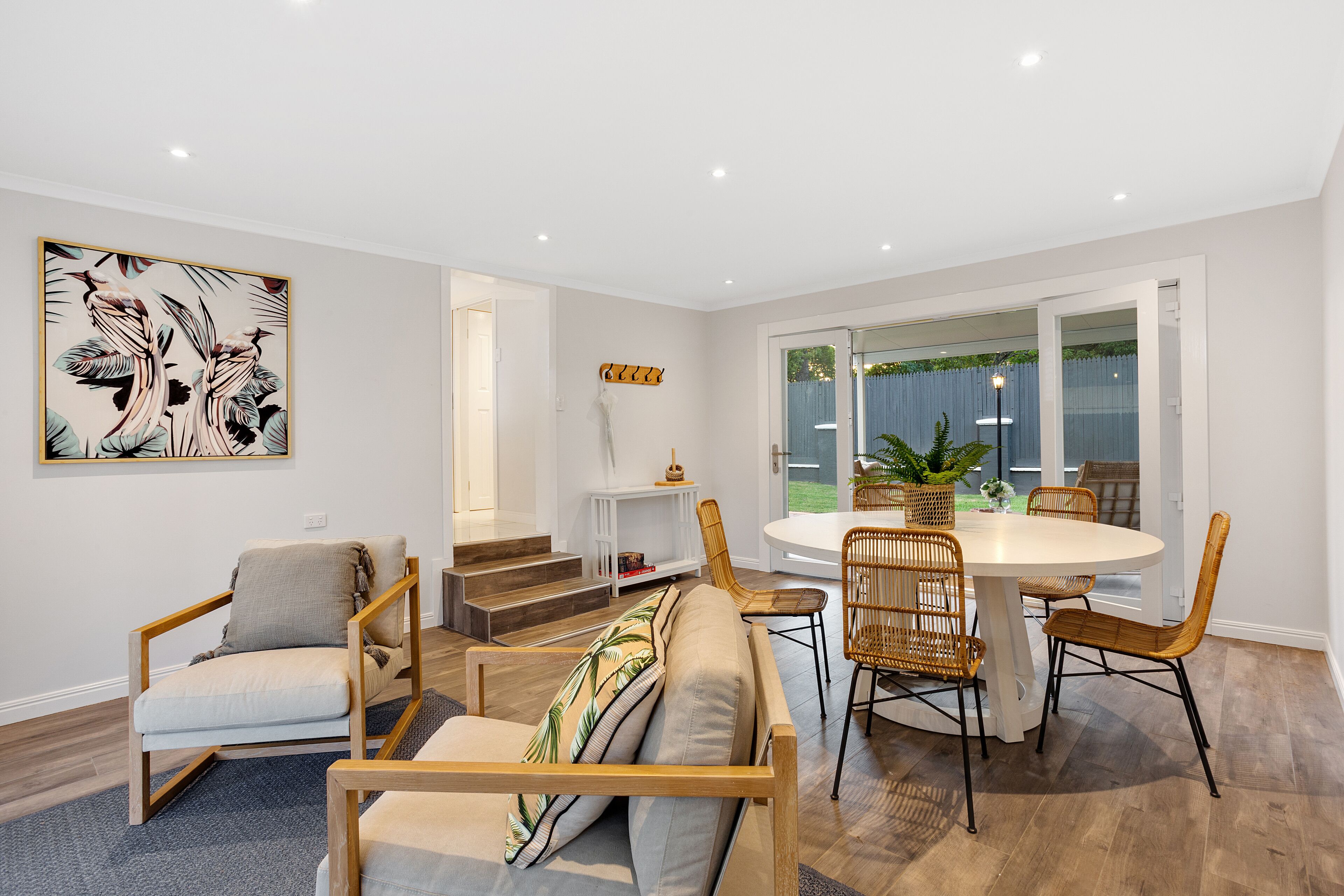 Una sala de estar moderna con sofá, sillas, una mesa de comedor y una escalera que sube a otro nivel.