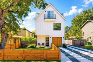 A modern two-story house with a front porch, a small garden, and a visible garage. - Sleeps 15 | East Austin, Garage, EV Charger (Austin)