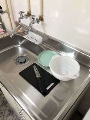 En diskho i rostfritt stål med en svart skärbräda, en grön tallrik och ett vitt durkslag.