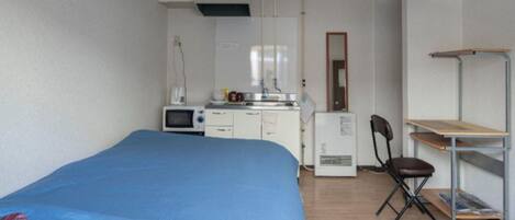 Una habitación pequeña con cama, kitchenette, escritorio y silla.