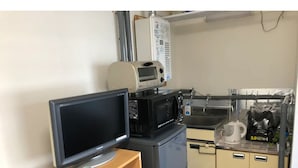 A compact kitchenette with a microwave, toaster, and a small refrigerator. A television is placed on a wooden stand. - Sapporo Apartment 0 (Sapporo)