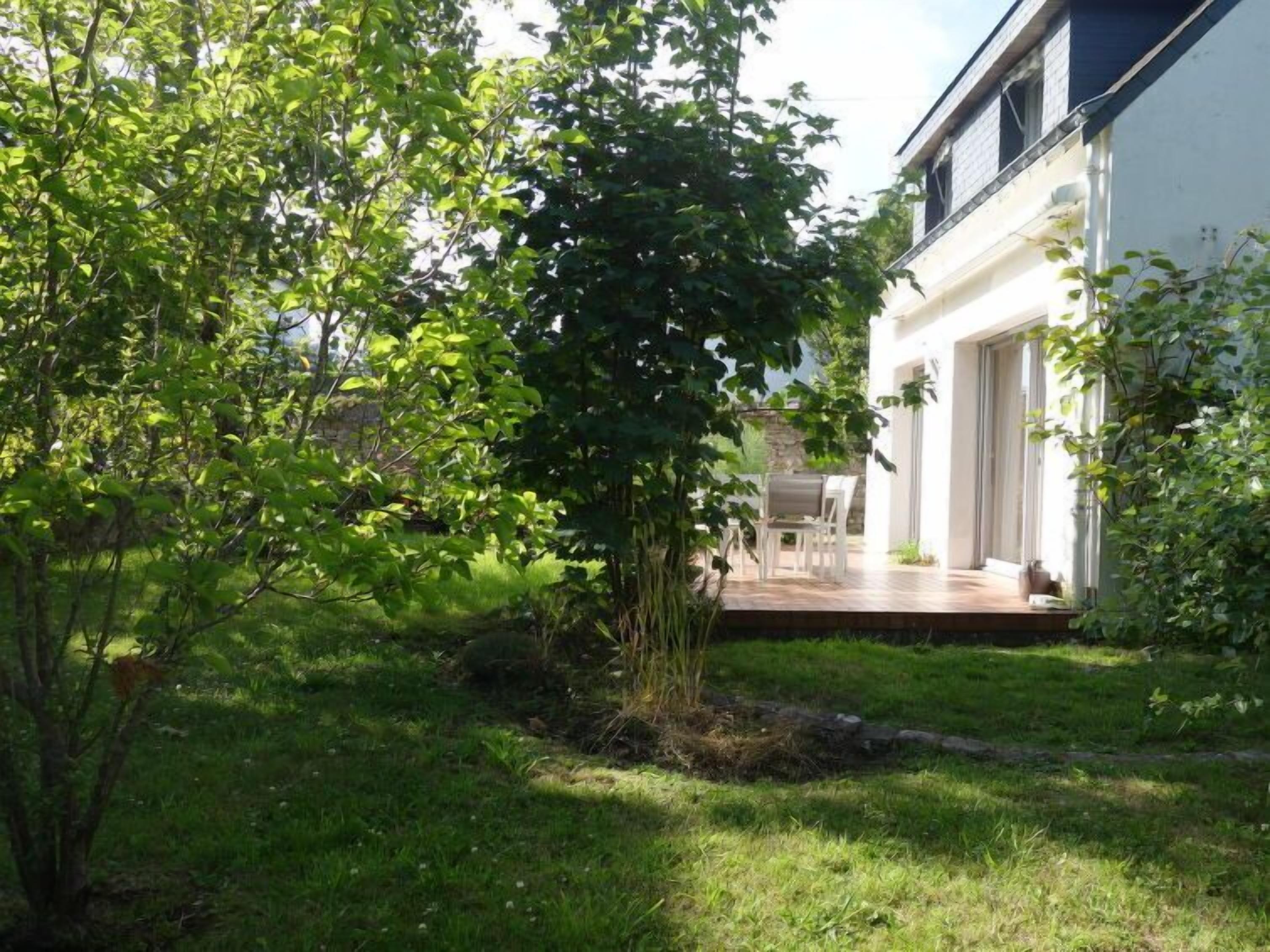 Ein modernes Haus mit einer überdachten Terrasse, einem Rasen und einem Baum.