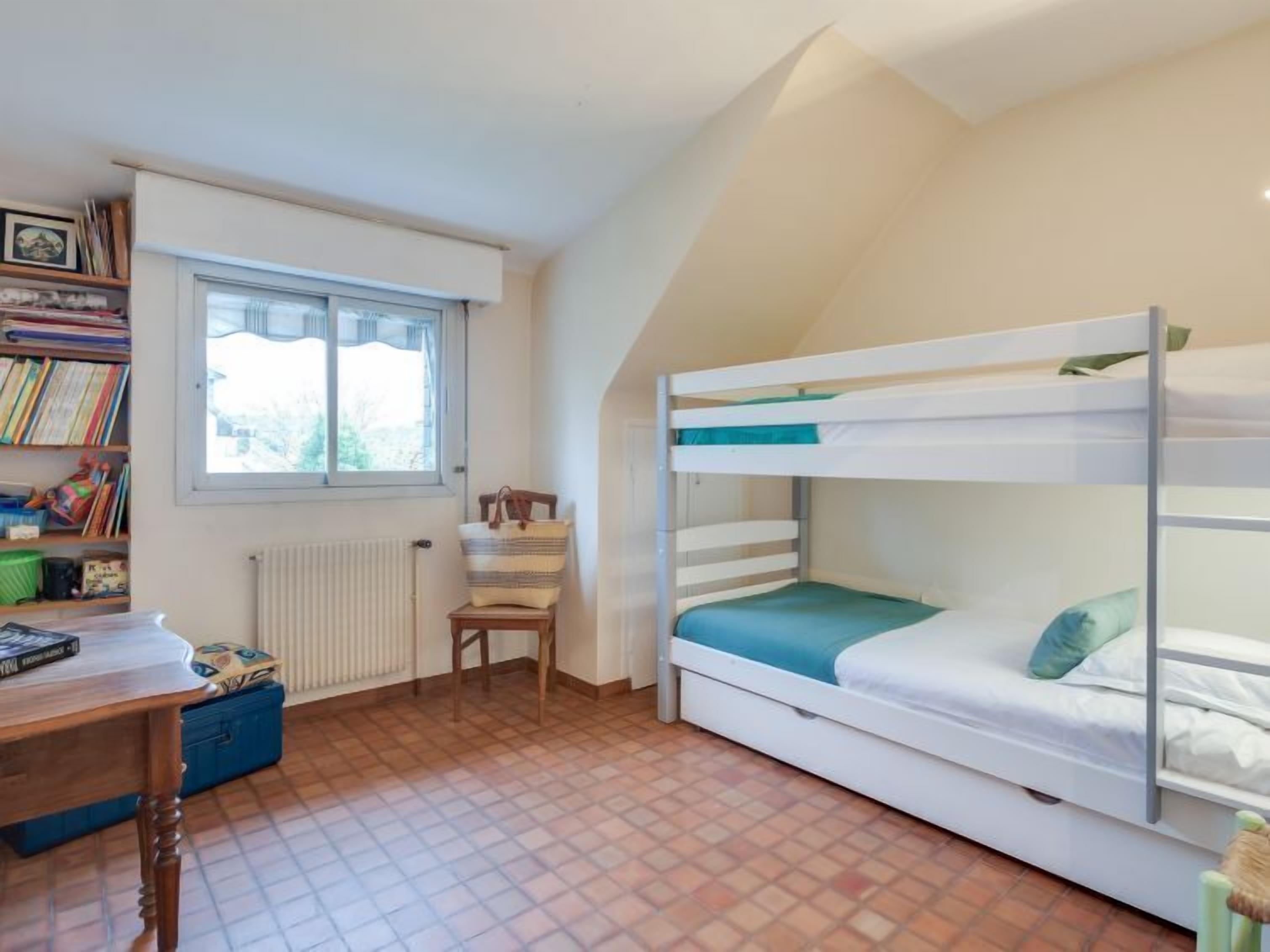 A child's bedroom with bunk beds, a desk, and a window.