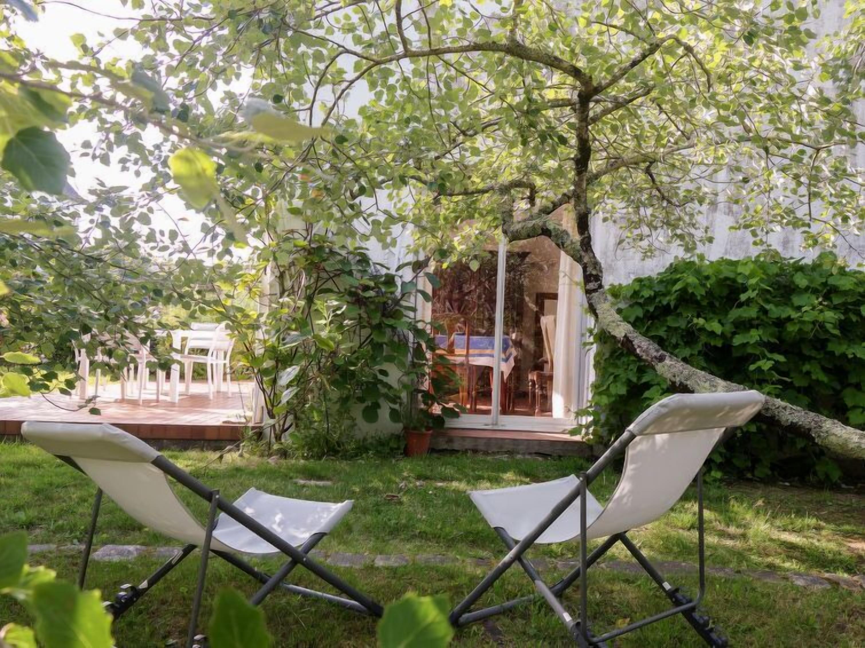 A garden with two white folding chairs, a white building with a covered patio, and lush greenery.