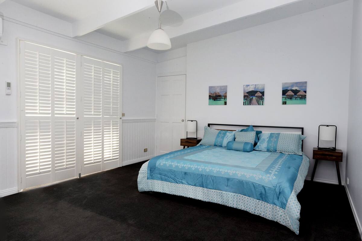 A bedroom with a large bed, white walls, and a ceiling fan. There are three framed pictures on the wall.
