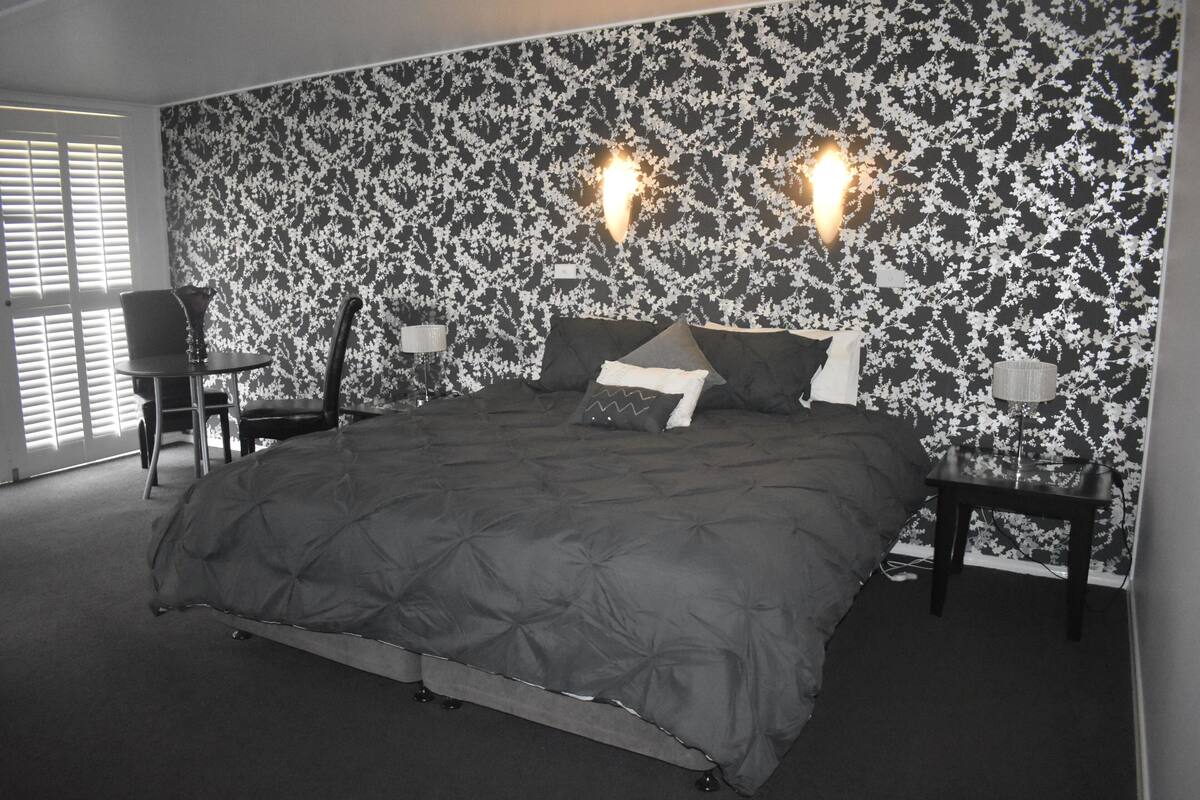 A bedroom with a large bed, two bedside tables, a chair, and a patterned wallpaper.