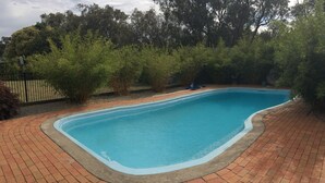 A rectangular swimming pool with a brick border, surrounded by trees and a fence. - Bellarine Spa Wellness & Retreat (Portarlington)