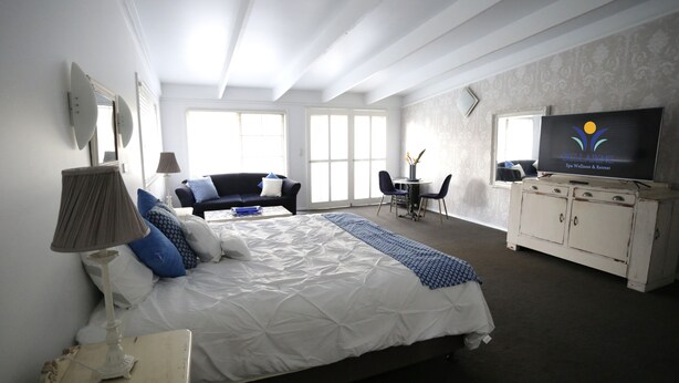 A bedroom with a bed, bedside table, lamp, dresser, TV, and a chair. - Bellarine Spa Wellness & Retreat (Portarlington)
